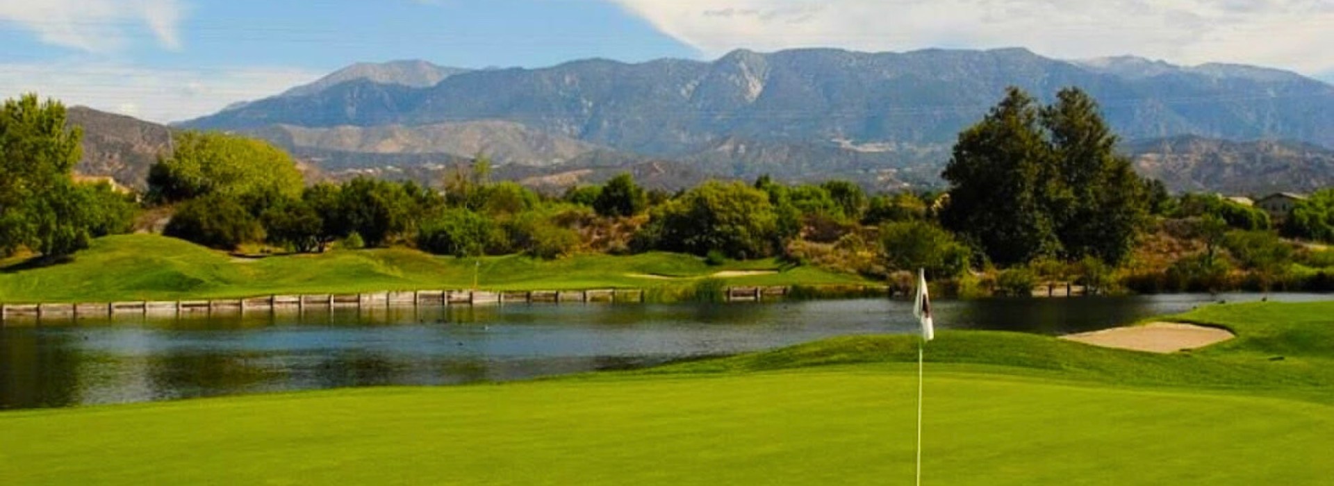View of golf course green with bunker and flag and mountains in distance